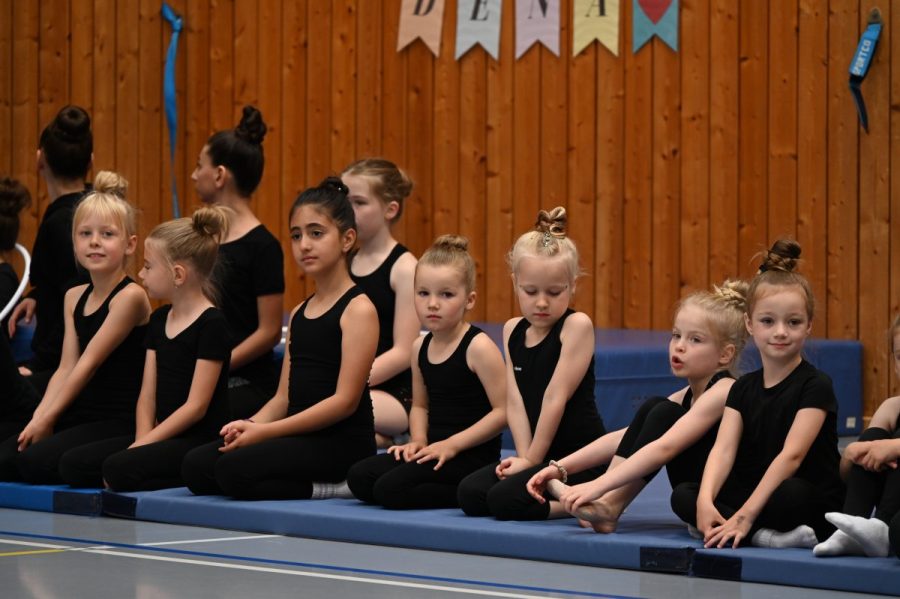 Eine Gruppe Mädchen sitzt in einer Reihe auf Matten in einer Sporthalle.