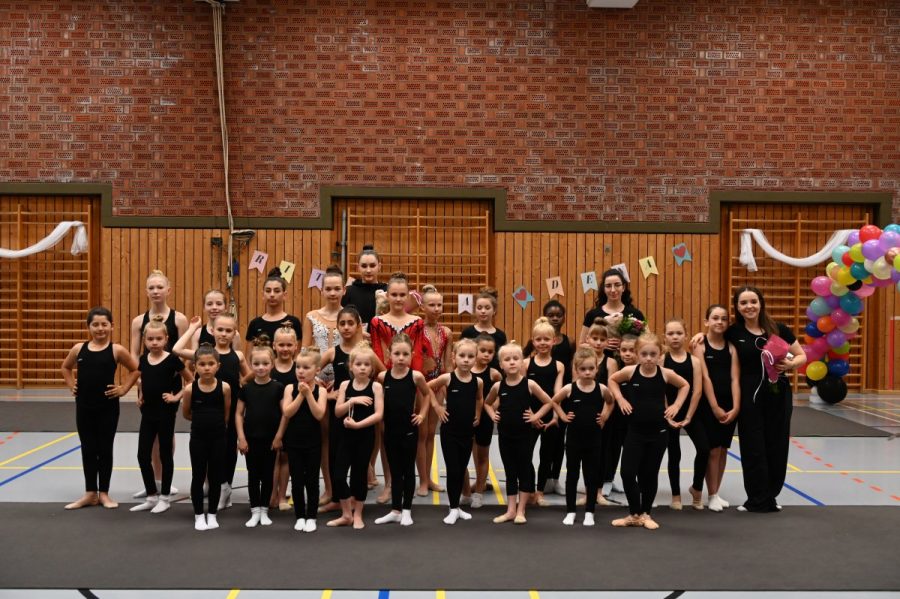 Eine große Gruppe von Gymnastinnen posiert gemeinsam in einer Sporthalle.