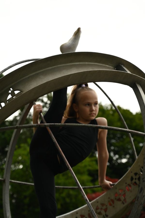 Eine Gymnastin zeigt eine Dehnübung im Inneren einer runden Metallskulptur.