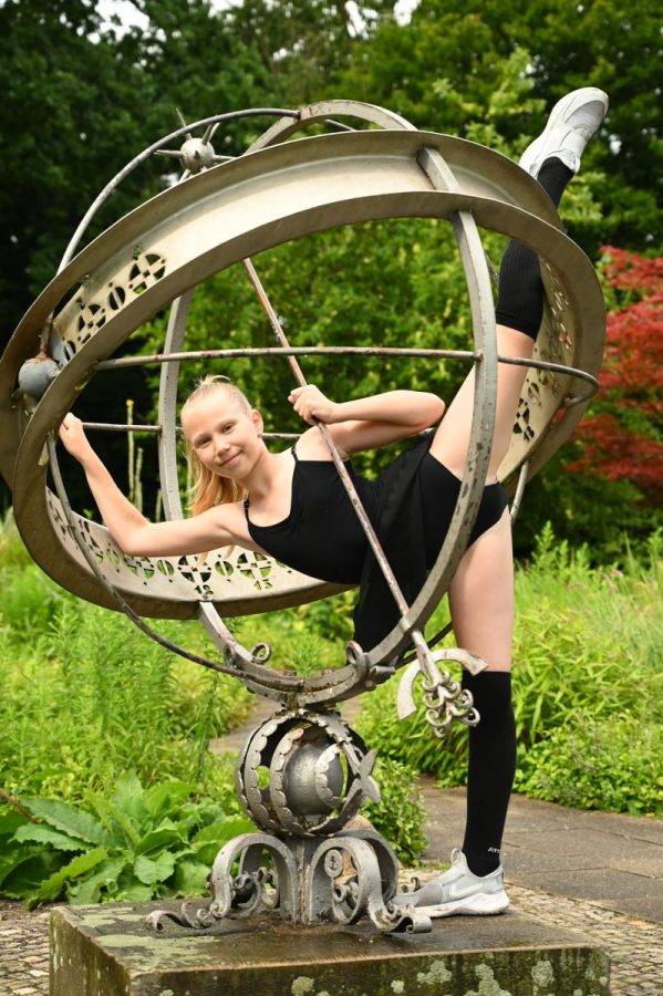 Eine Gymnastin zeigt in einem Park einen Spagat am metallischen Ringmodell.
