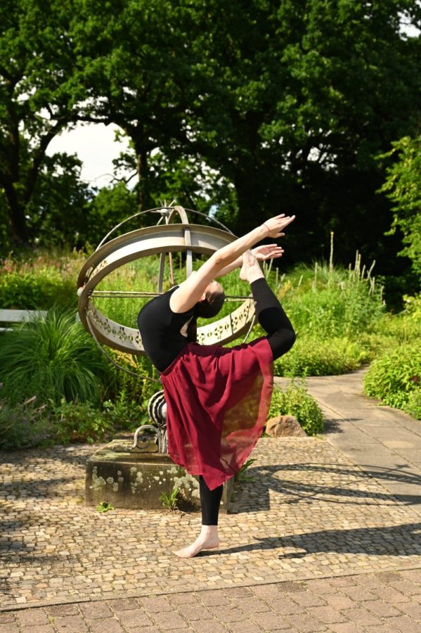 Eine Gymnastin zeigt eine Standwaage am metallischen Ringmodell im Freien.