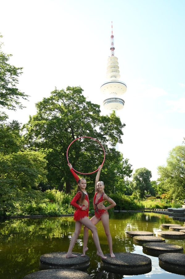 Zwei Gymnastinnen mit einem Reifen im Freien an einem Gewässer mit einem Fernsehturm im Hintergrund.