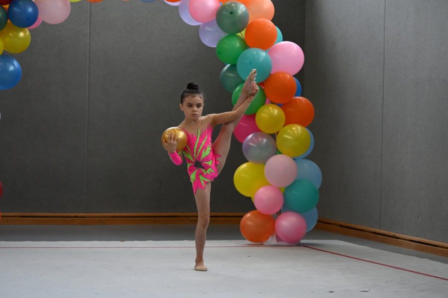 Eine Gymnastin zeigt vor einem Ballonbogen eine Standwaage mit einem Ball.