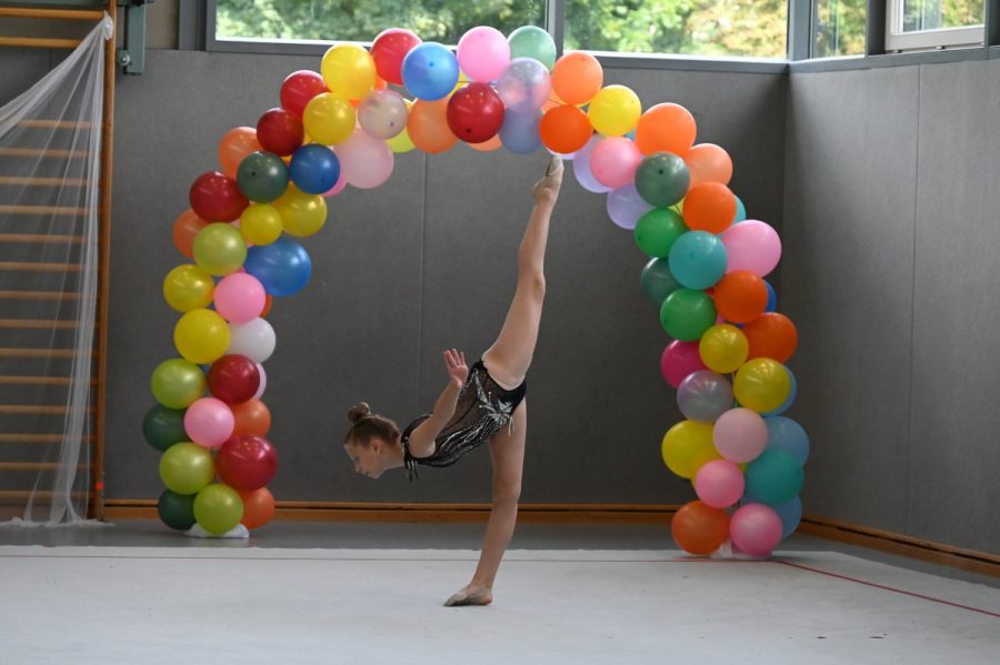 Eine Gymnastin führt vor einem bunten Ballonbogen eine Standwaage vor.