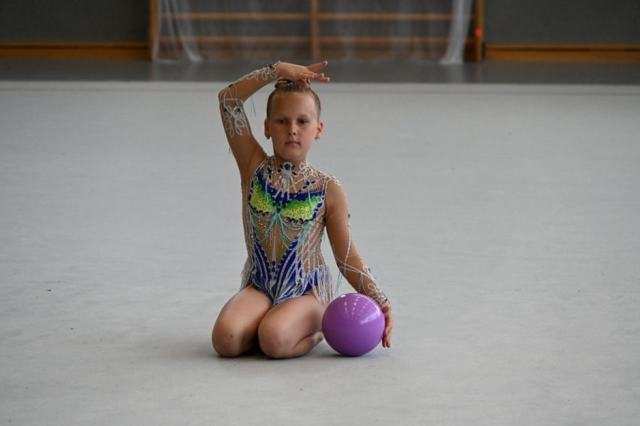 Eine Gymnastin kniet auf dem Hallenboden und hält einen Ball in der Hand.
