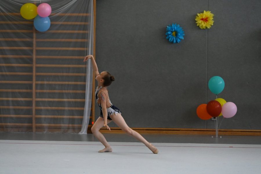 Eine Gymnastin in Sporthose und Trikot nimmt in der Halle eine Tanzpose ein.