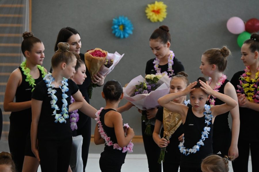 Eine Gruppe Mädchen mit Blumensträußen und Blütenkränzen in einer Turnhalle.