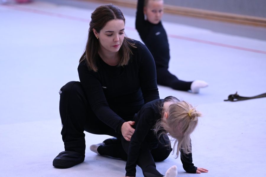 Eine Trainerin unterstützt eine junge Gymnastin beim Dehnen in der Halle.