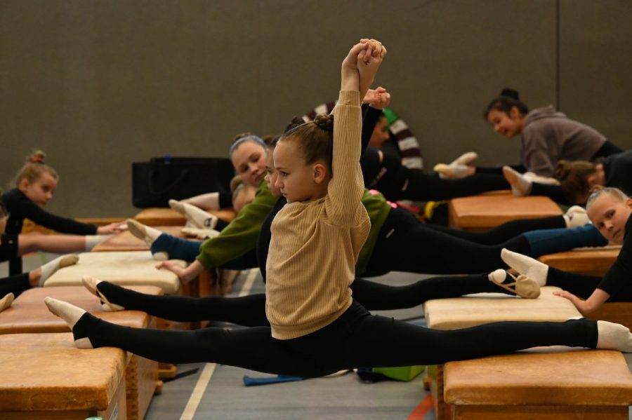 Mehrere Gymnastinnen machen beim Dehnen auf Kästen in einer Sporthalle den Spagat.