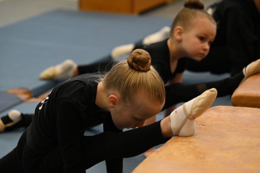 Zwei Gymnastinnen beim Dehnen und Spagat auf Kästen in der Sporthalle.