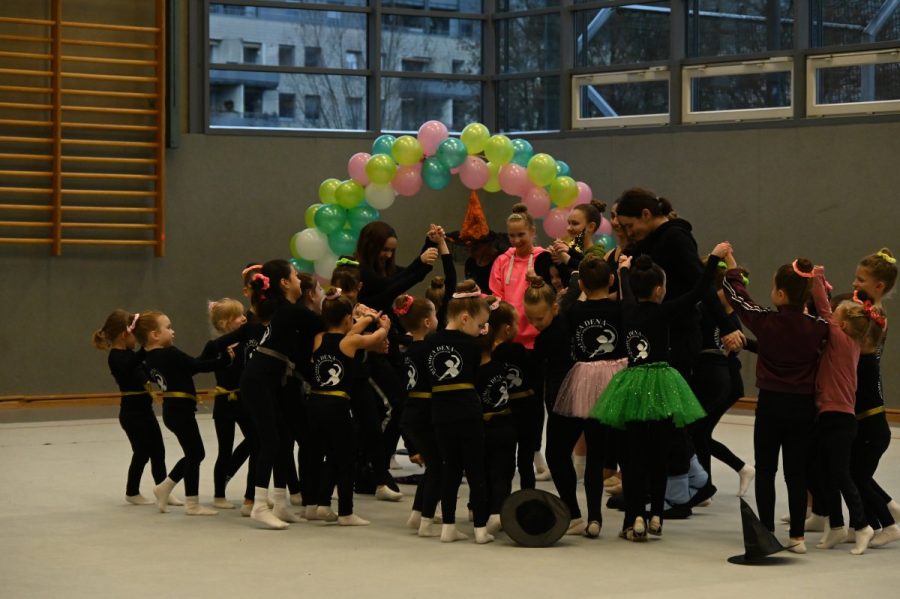 Eine große Gruppe Kinder steht unter einem bunten Ballonbogen in einer Halle.