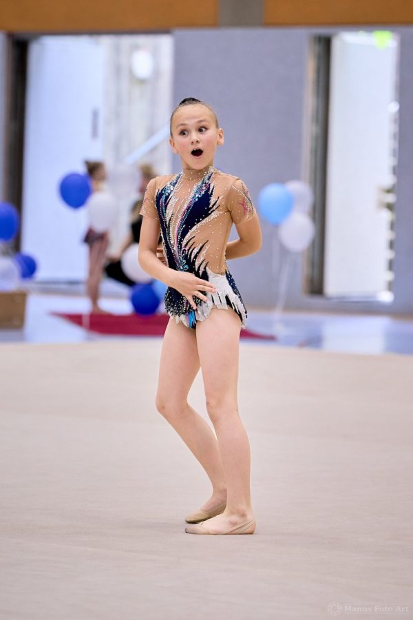 Eine Gymnastin steht in einer Sporthalle mit geöffnetem Mund und macht eine Handbewegung.