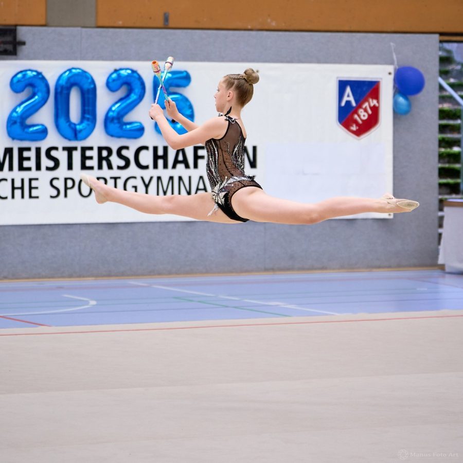 Eine Gymnastin zeigt einen Spagat-Sprung mit Keulen.