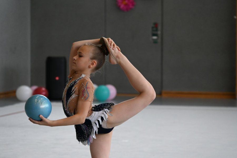 Eine Gymnastin hält einen Ball und führt eine Übung mit gebeugtem Rücken aus.