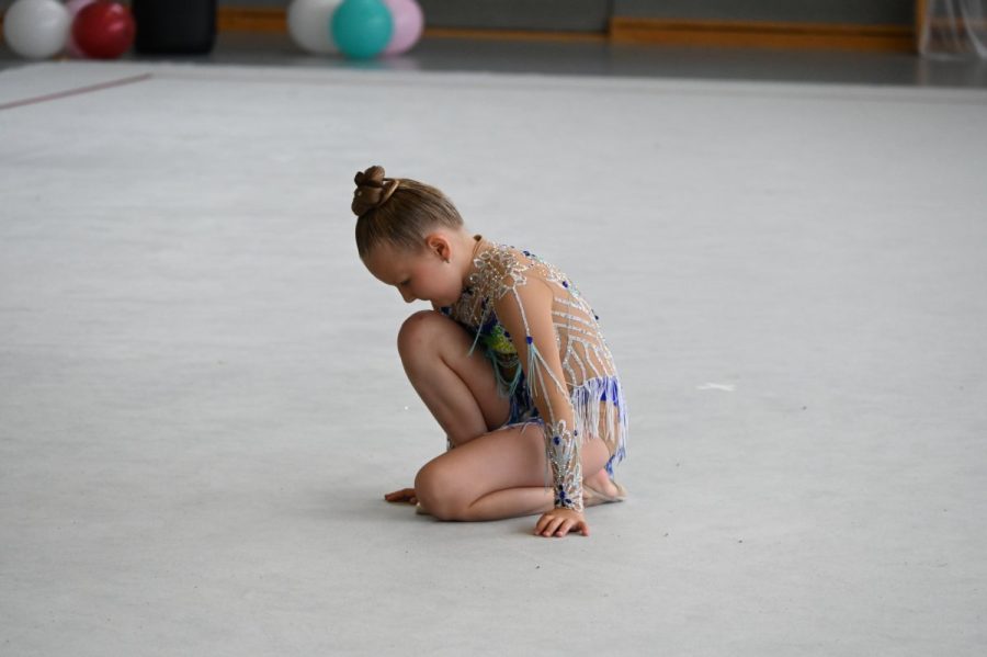 Eine Gymnastin sitzt in einer Pose auf dem Hallenboden.