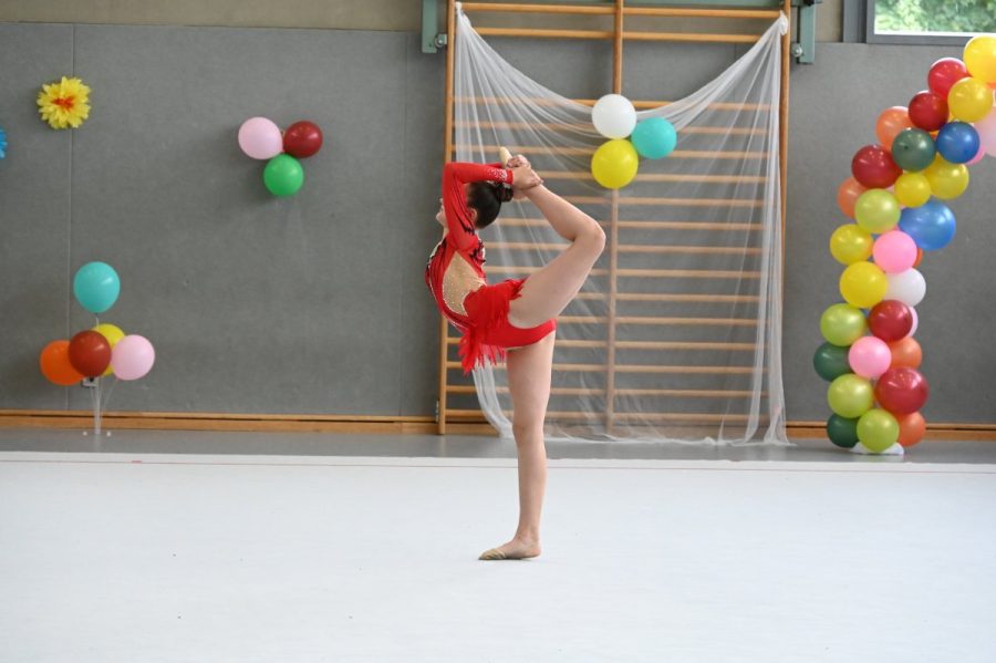 Eine Gymnastin zeigt in einer Turnhalle eine Standwaage mit erhobenem Bein.