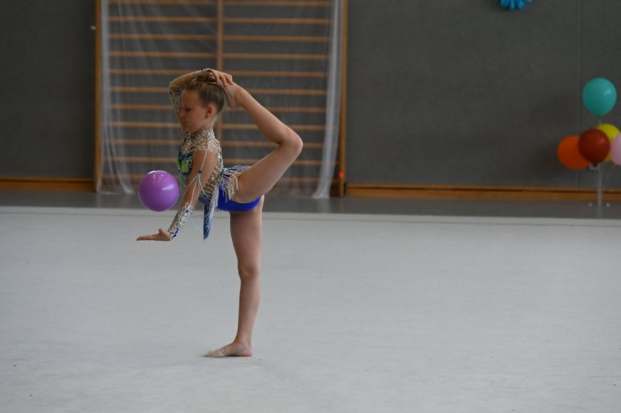 Eine Gymnastin zeigt in der Halle mit einem Ball eine Standstandwaage mit Rumpfbeuge.