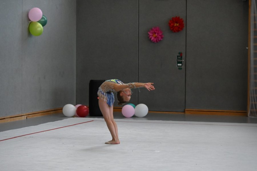 Eine Gymnastin steht in der Halle in einer tiefen Rückbeuge.