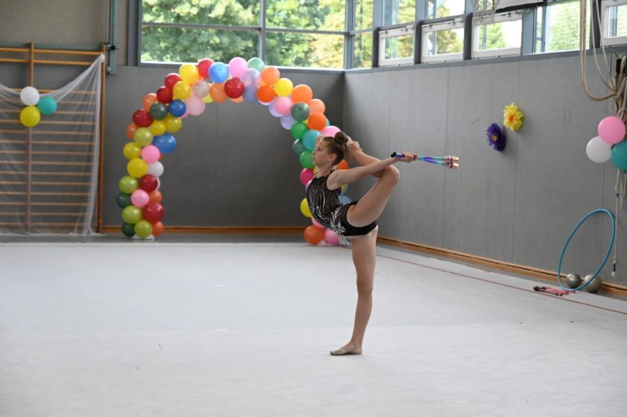 Eine Gymnastin zeigt in der Halle mit Keulen eine Standwaage.