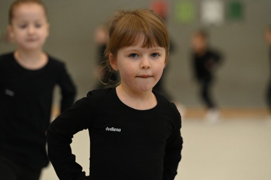 Ein Mädchen im Sportdress steht in der Halle, im Hintergrund weitere Kinder.