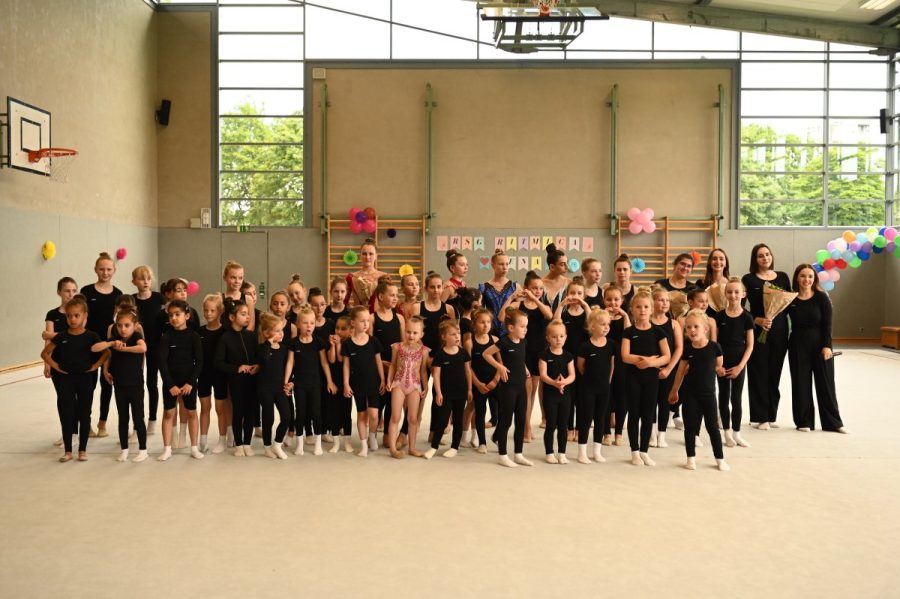Große Gruppe von Gymnastinnen und Trainerinnen versammelt in einer Sporthalle.