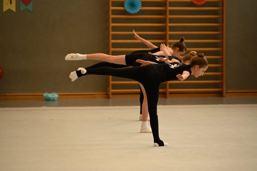 Mehrere Gymnastinnen stehen in einer Sporthalle in der Standwaage.