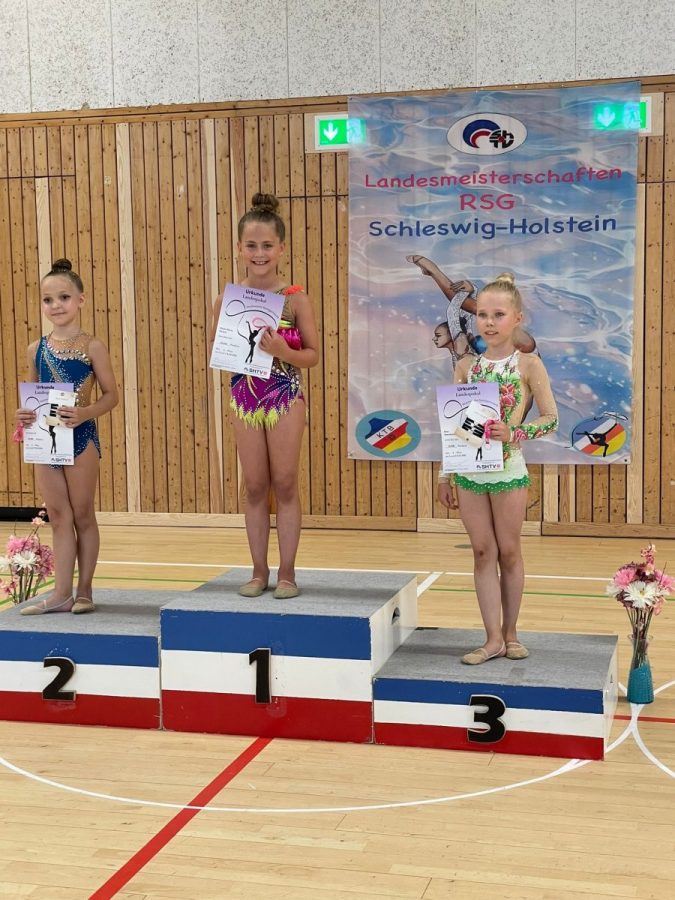 Three gymnasts present their certificates on the podium.