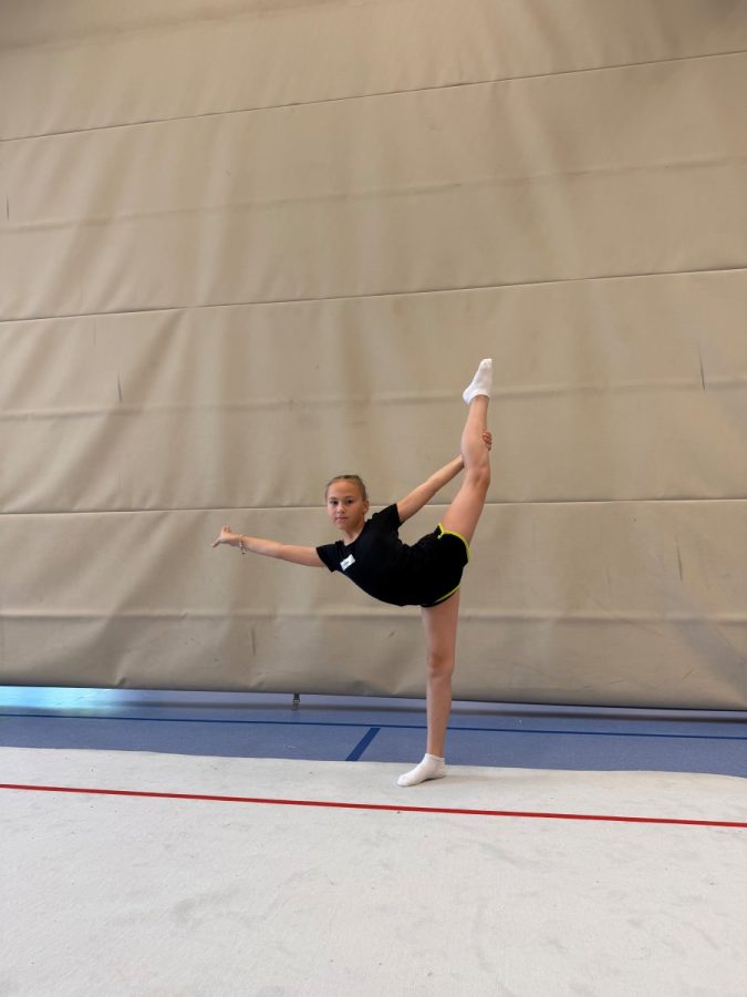 Eine junge Gymnastin steht in einer Dehnung auf der Matte in der Sporthalle.